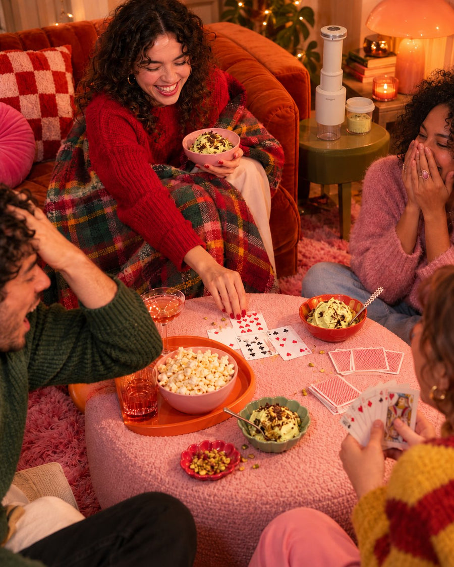 Friends playing cards around a pink pouf with bowls of pistachio ice cream, the CompactCream on the side table